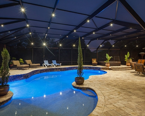 Pool with a large deck and screen enclosure with nebula light on the enclosure and in the pool
